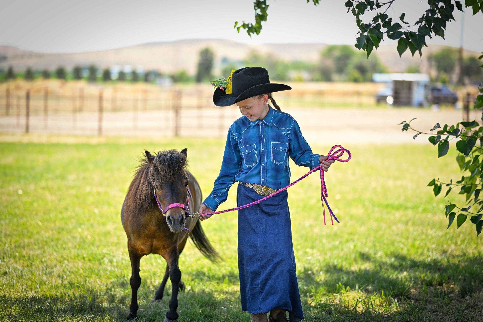 A young girl is walking a pony on a leash in a field.