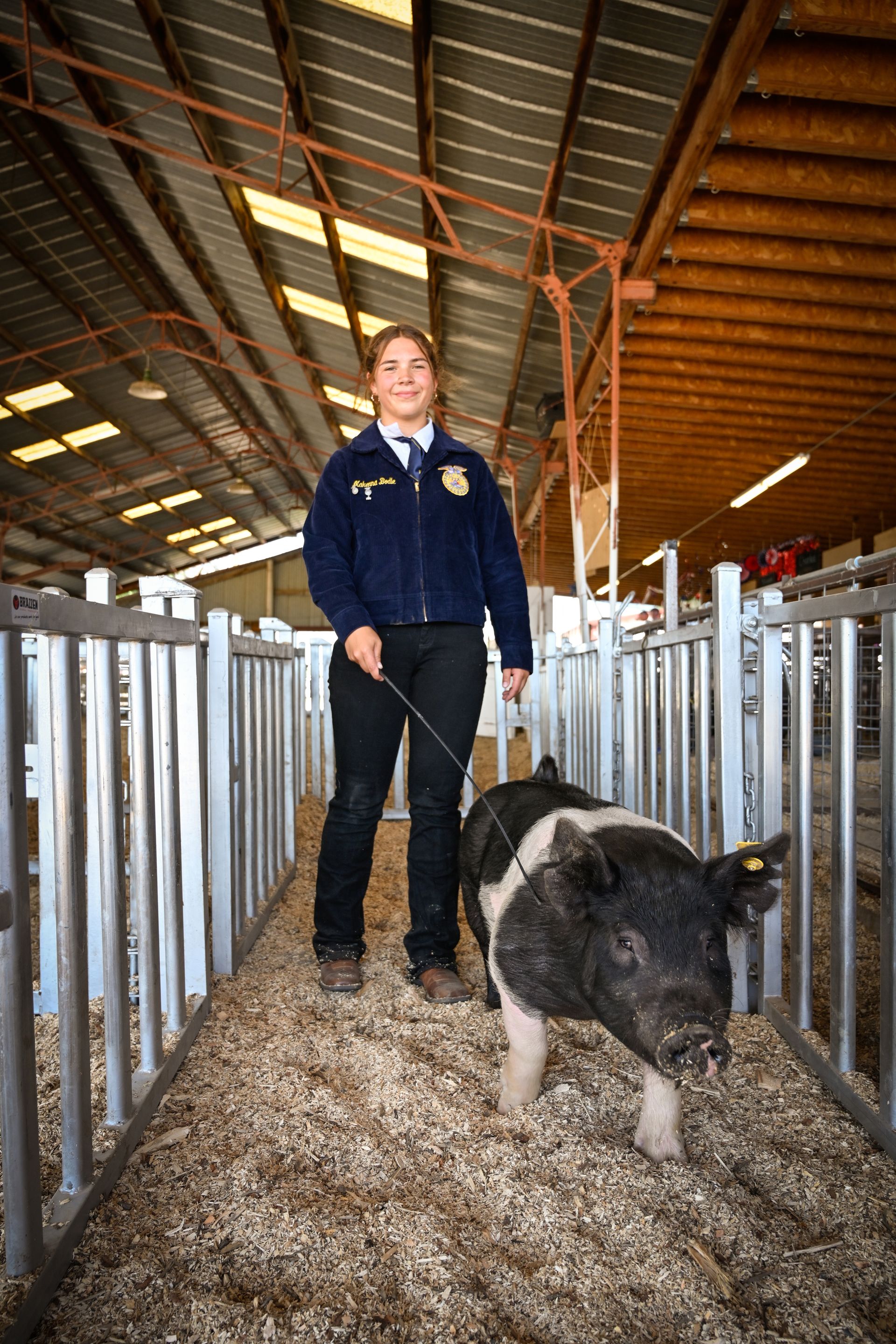 A woman is standing next to a pig in a pen.