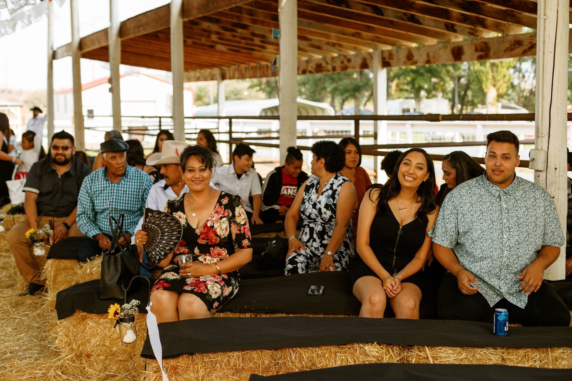 A group of people are sitting on hay bales under a covered area.