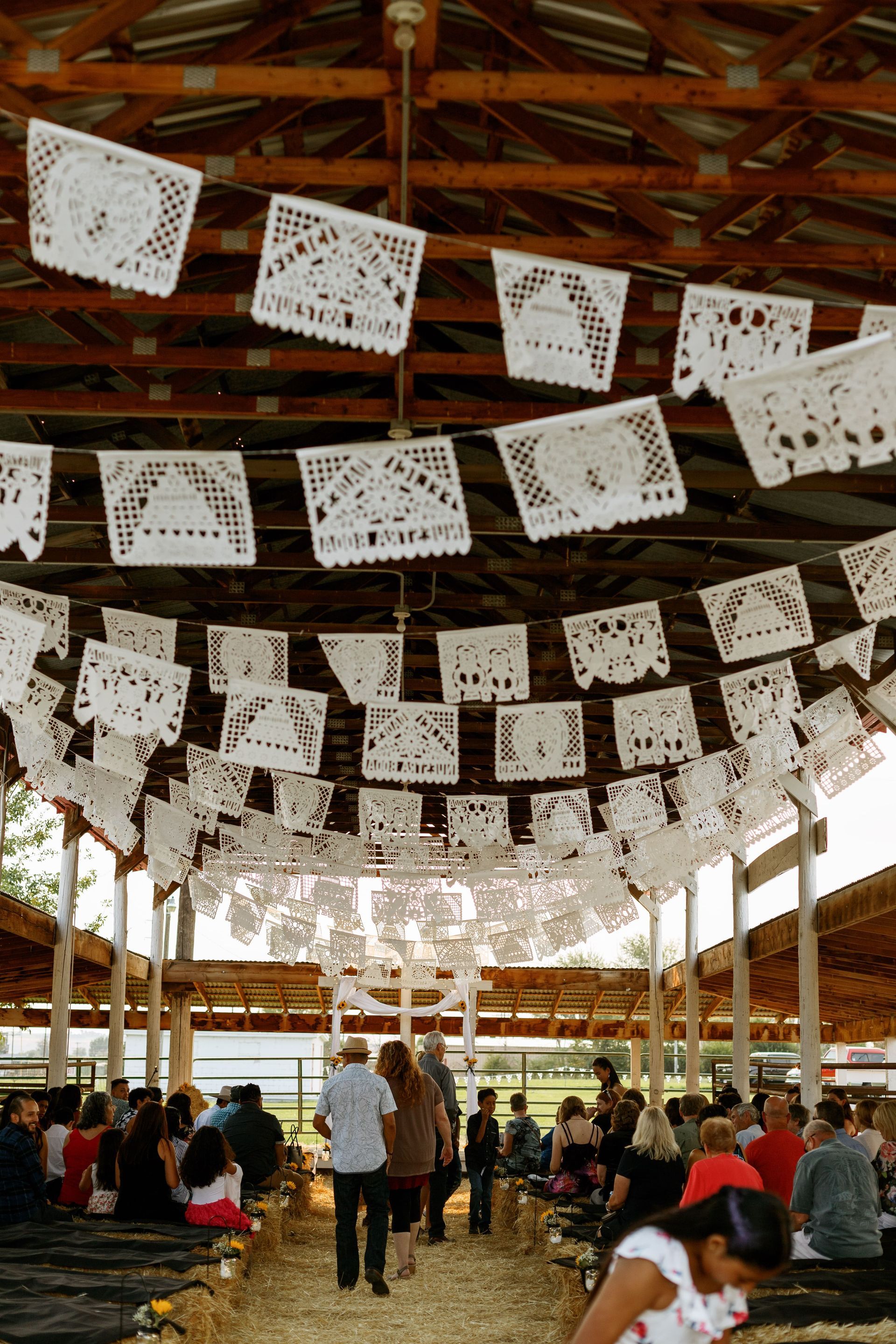 A group of people are gathered under a covered area with paper flags hanging from the ceiling.