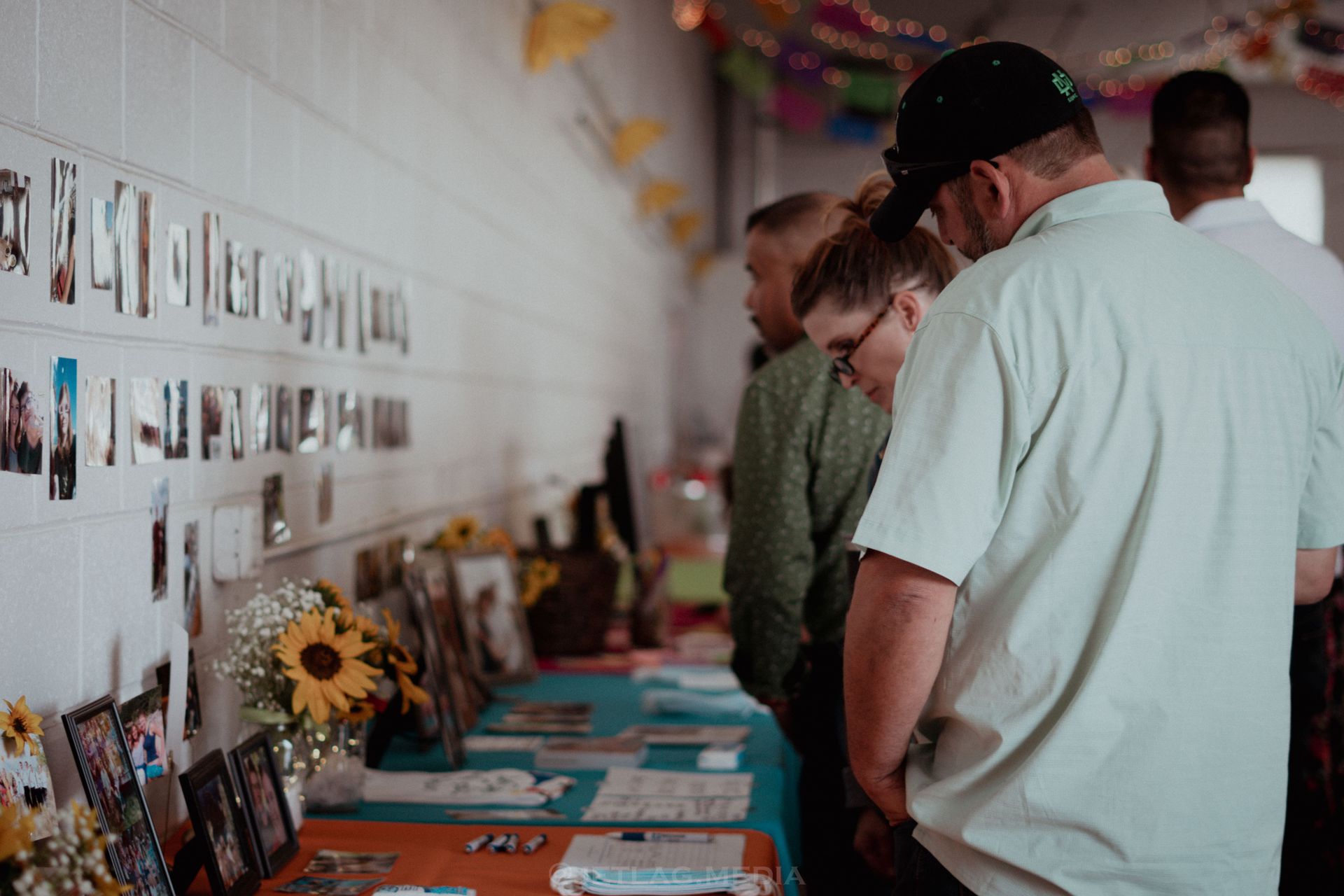 A group of people are standing around a table looking at pictures on a wall.