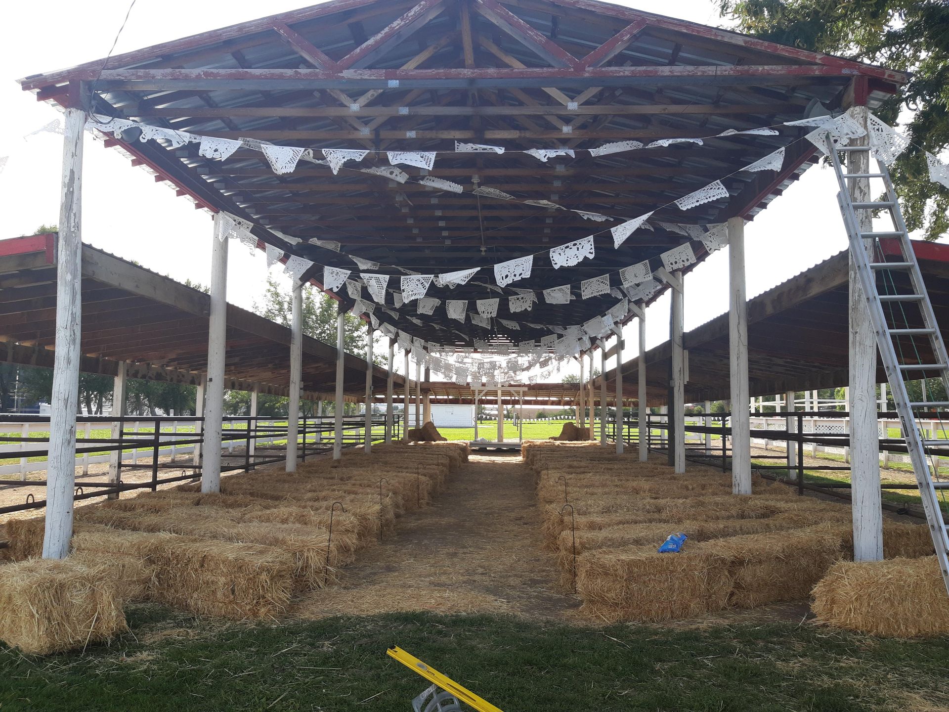 A row of hay bales under a roof with a ladder in the foreground.