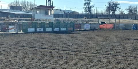 A dirt field with a fence and a building in the background.