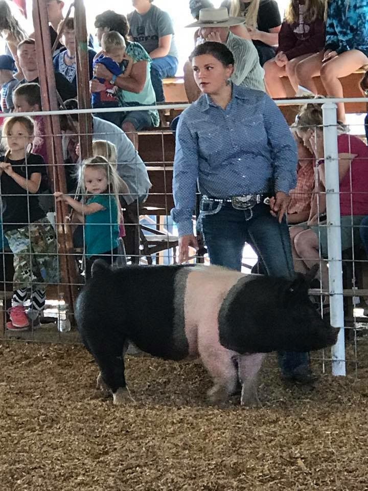 A woman is standing next to a pig in a pen at a show.