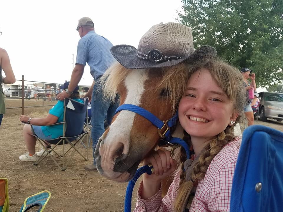 A girl wearing a cowboy hat is holding a pony