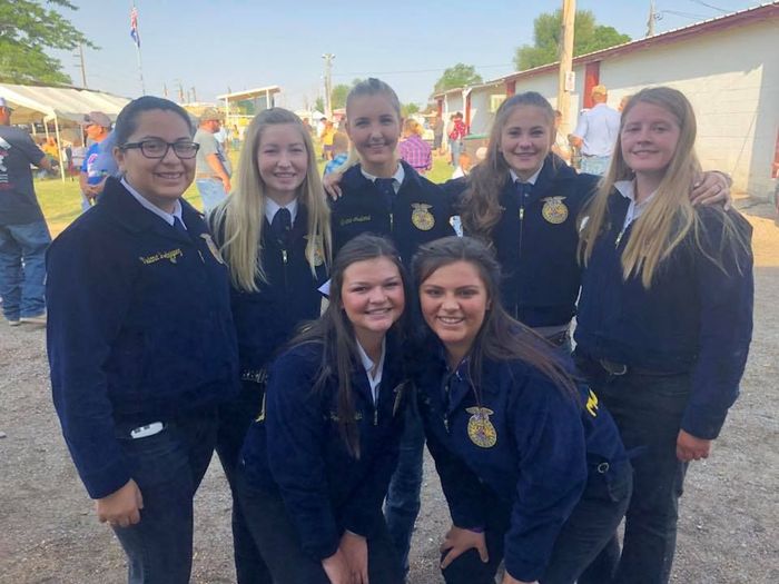Group of seven FFA members smiling, wearing blue jackets outdoors.