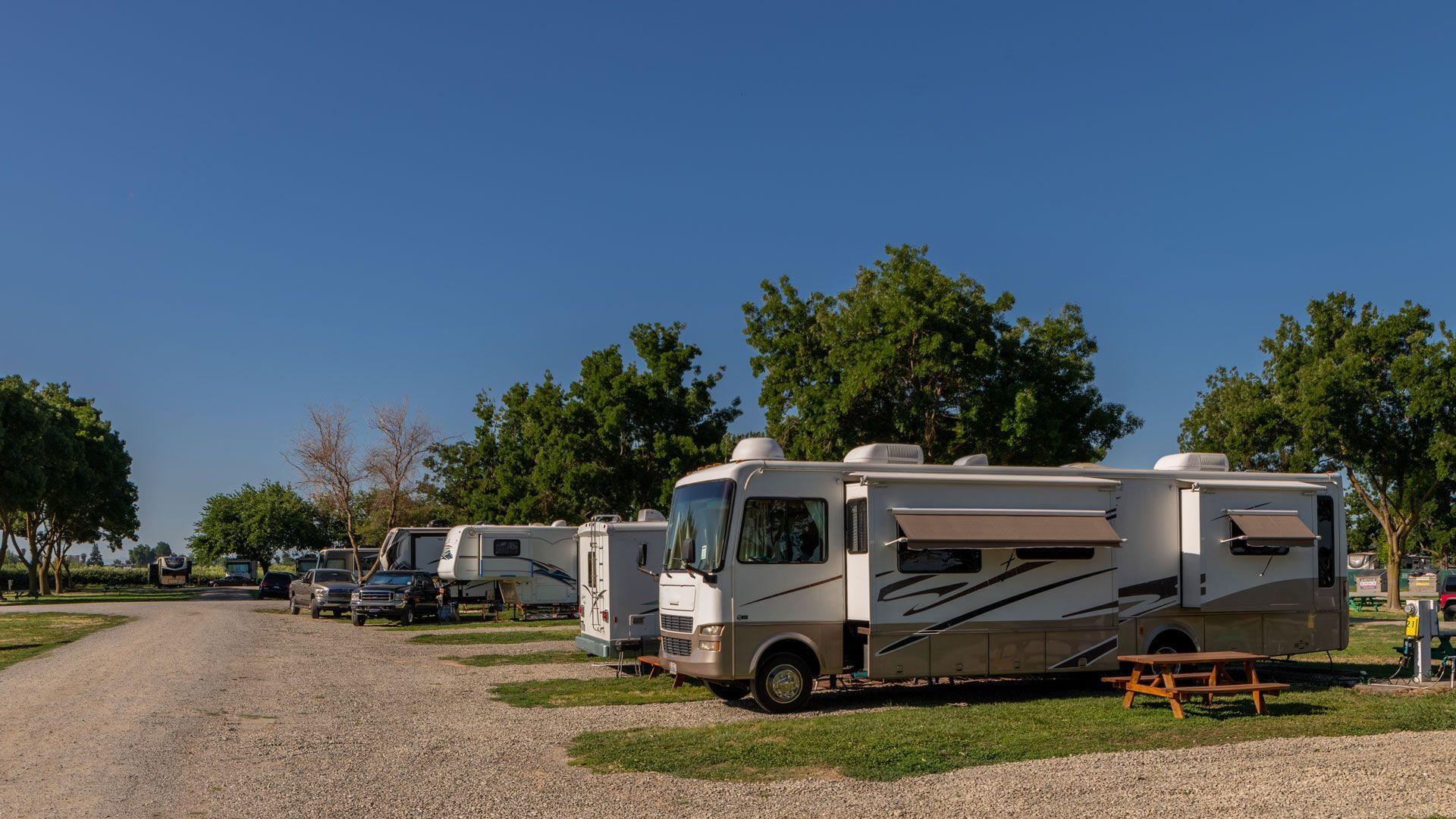 RV park with several motorhomes and trailers parked on gravel, under a clear blue sky.