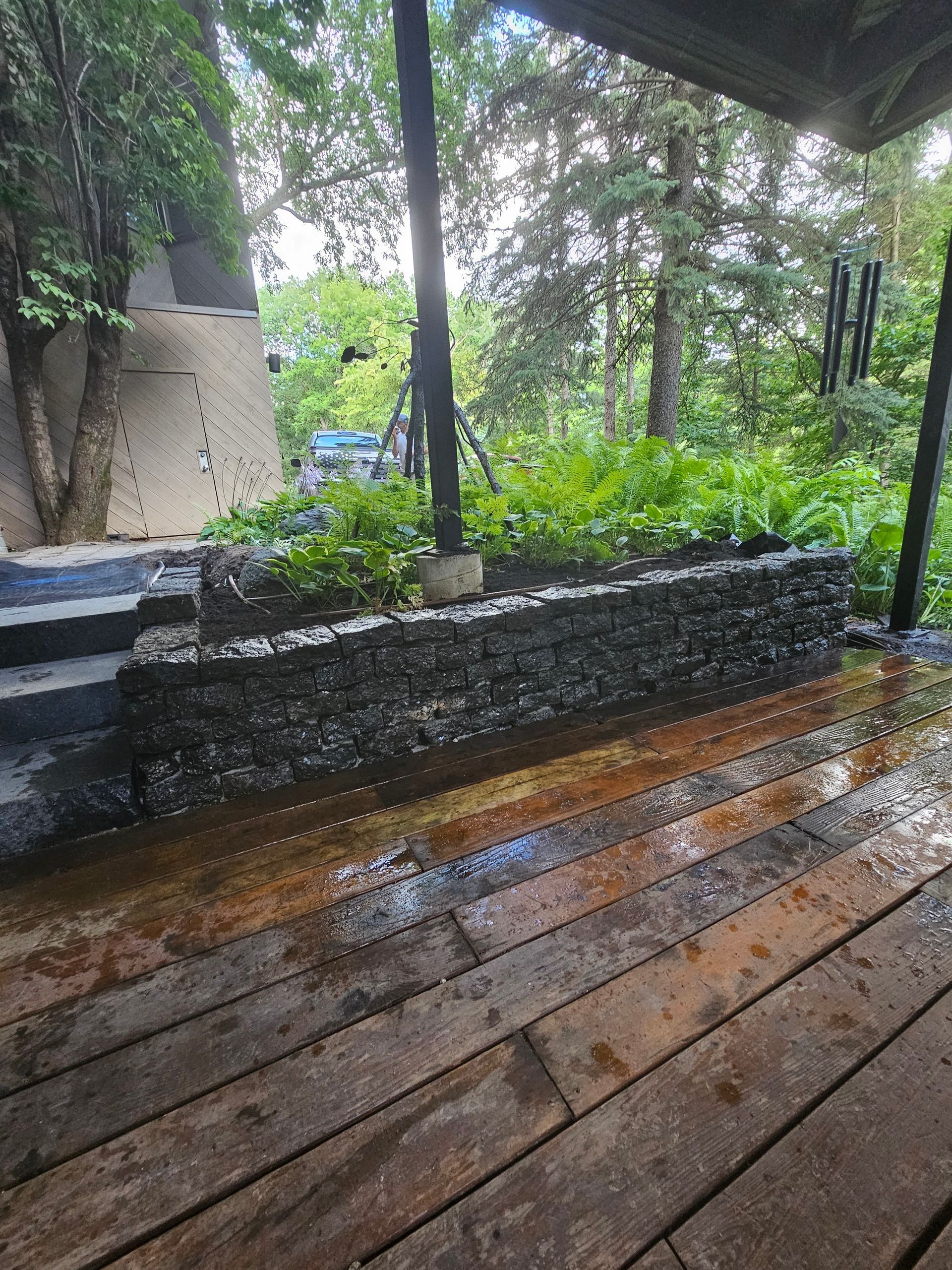 A wooden deck with a stone wall and trees in the background.