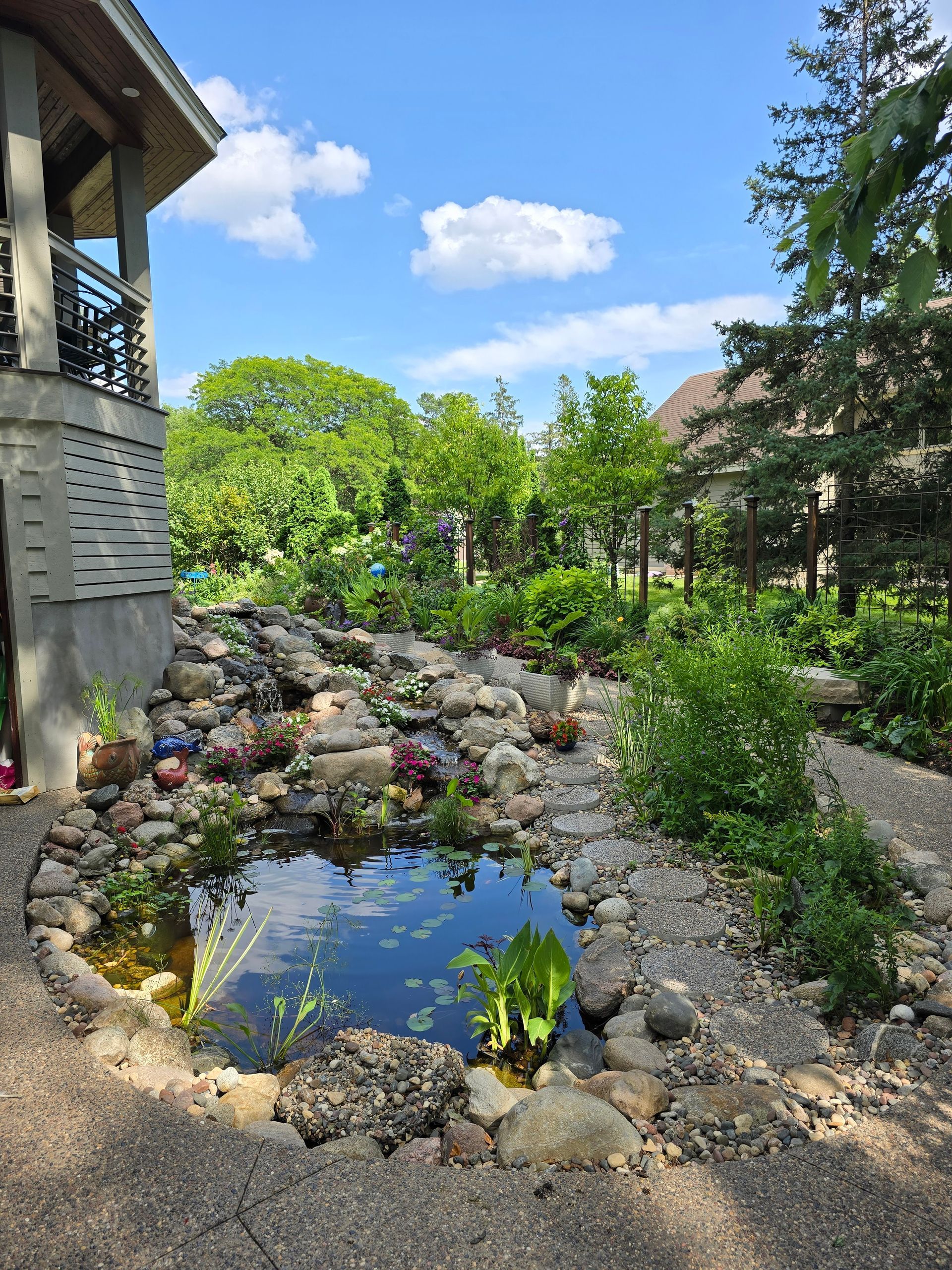 There is a pond in the middle of a garden next to a house.
