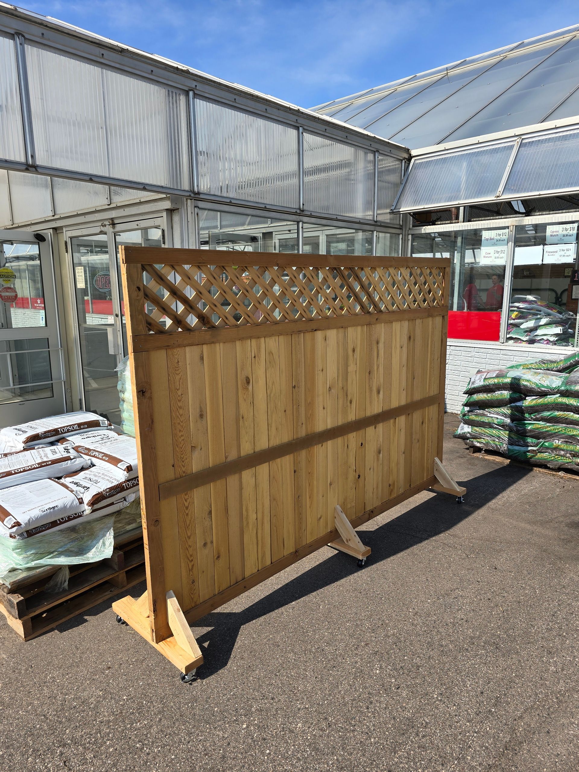 A wooden fence is sitting in front of a greenhouse.