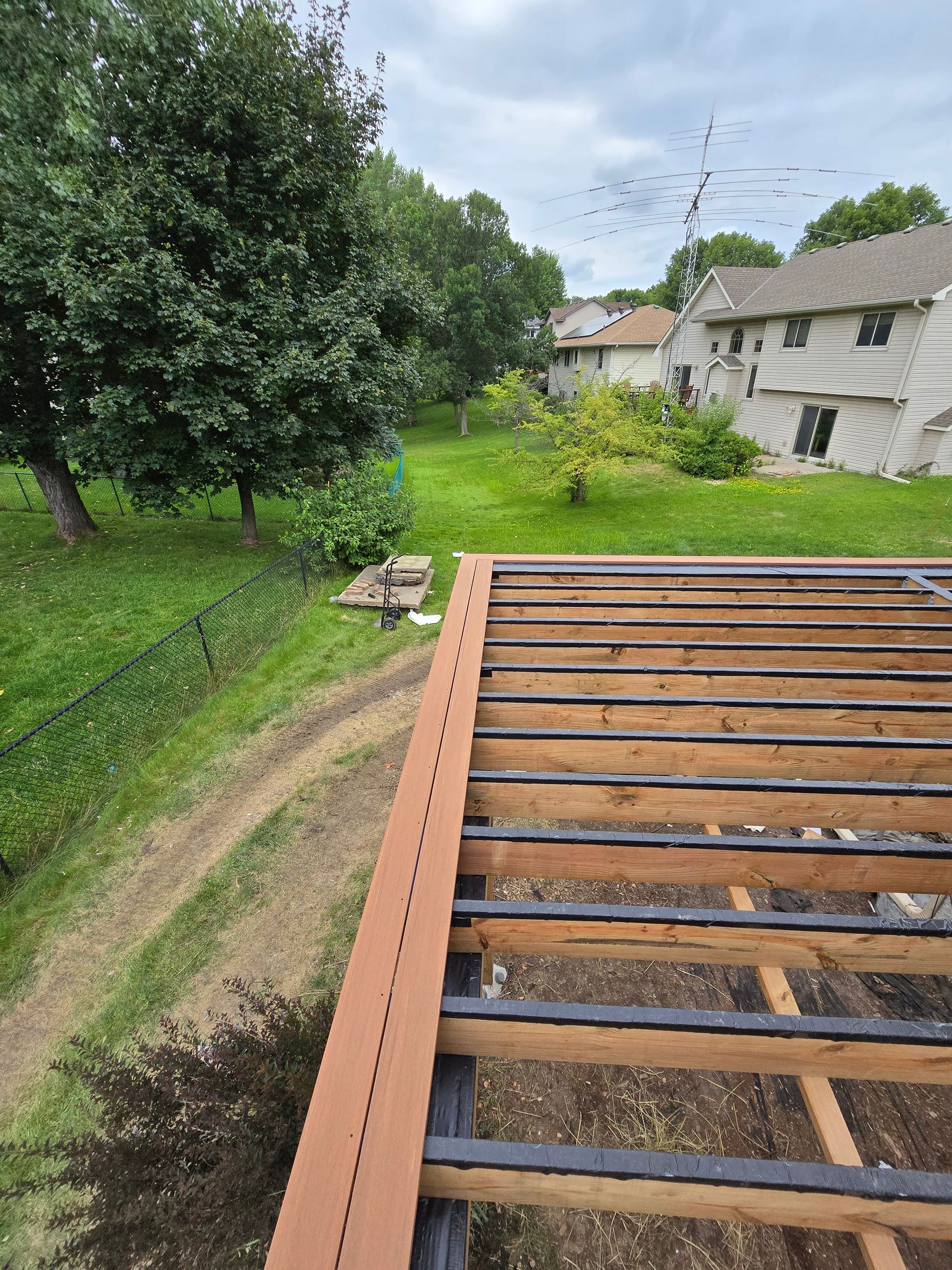 A wooden deck is being built in a backyard with a house in the background.