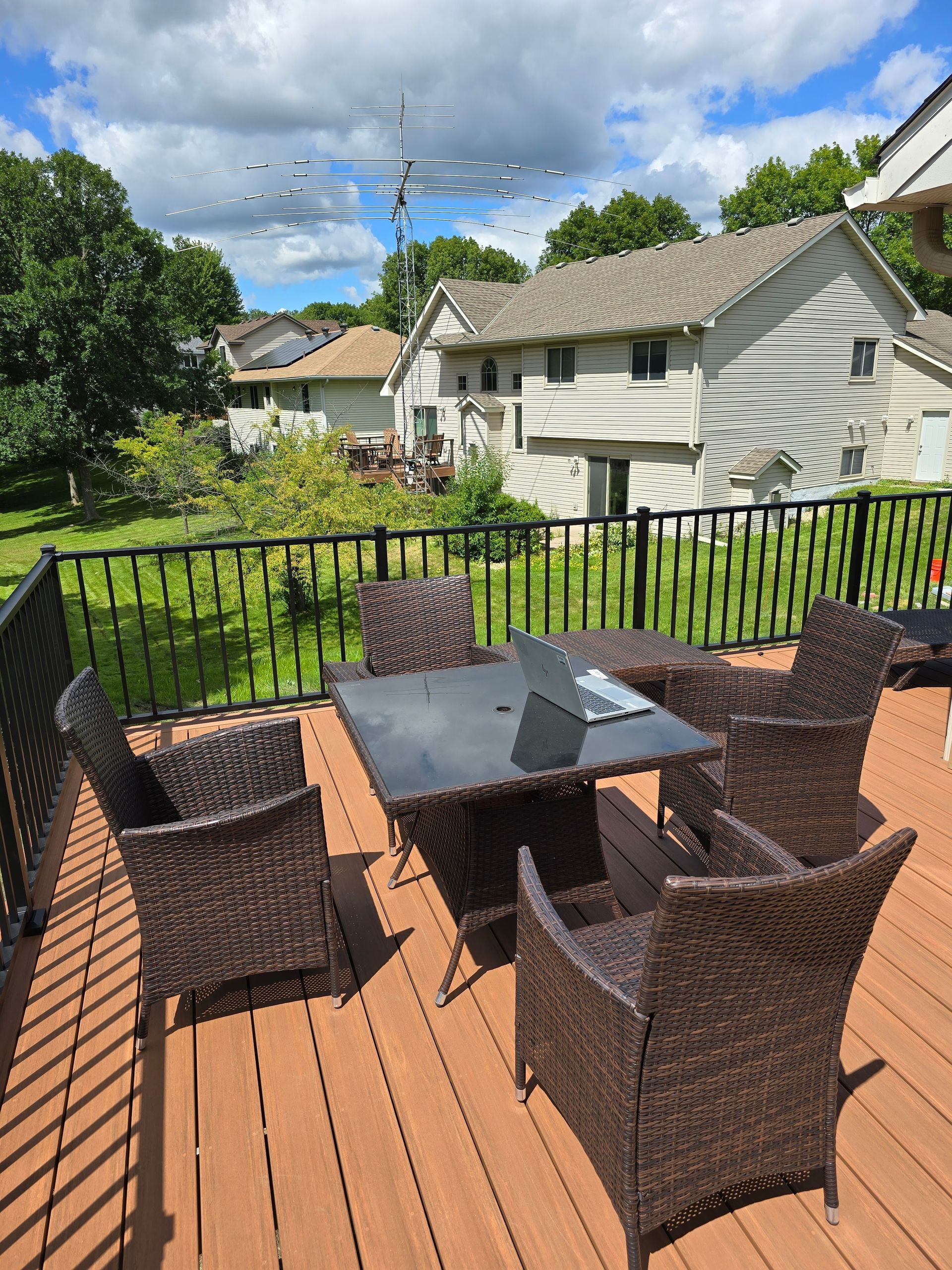 A deck with wicker chairs and a table with a laptop on it