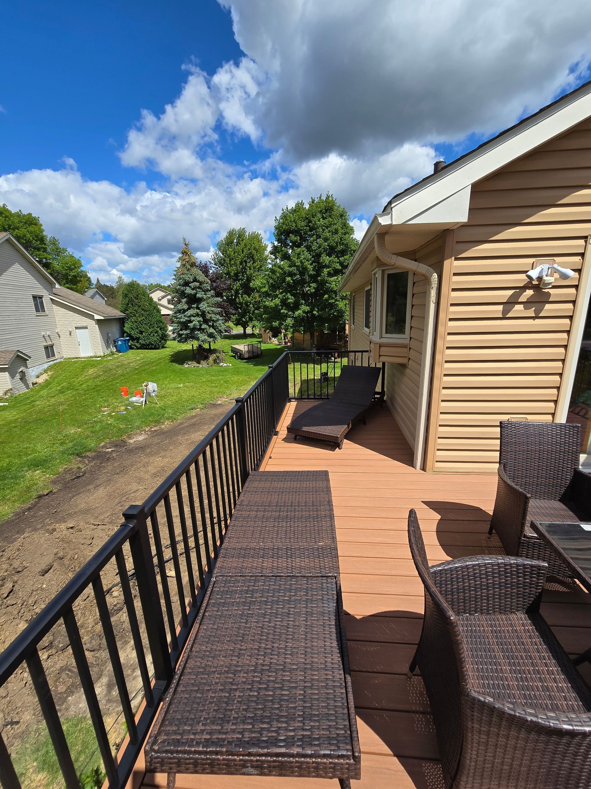 There is a deck with wicker furniture on it and a house in the background.
