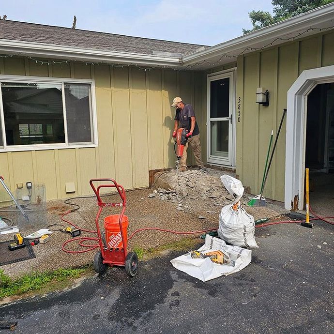 A man is using a drill in front of a house