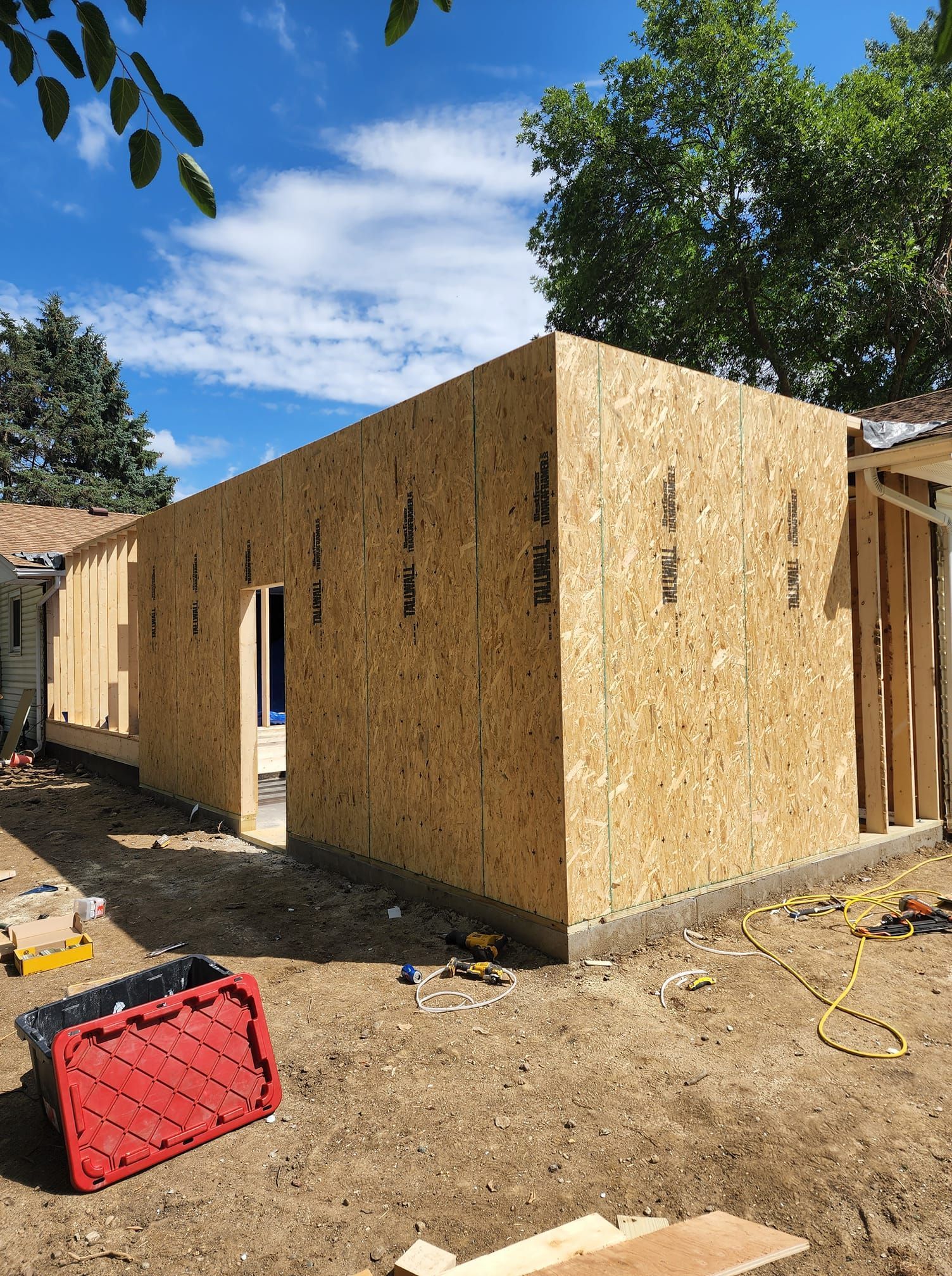 A red toolbox is sitting in the dirt in front of a house under construction.