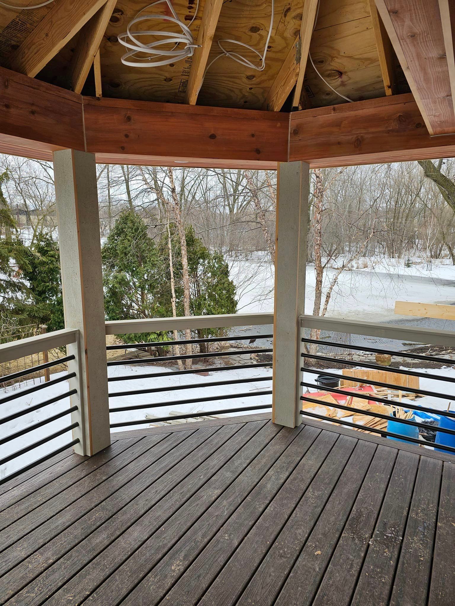 A wooden deck with a railing and a view of a snowy forest.