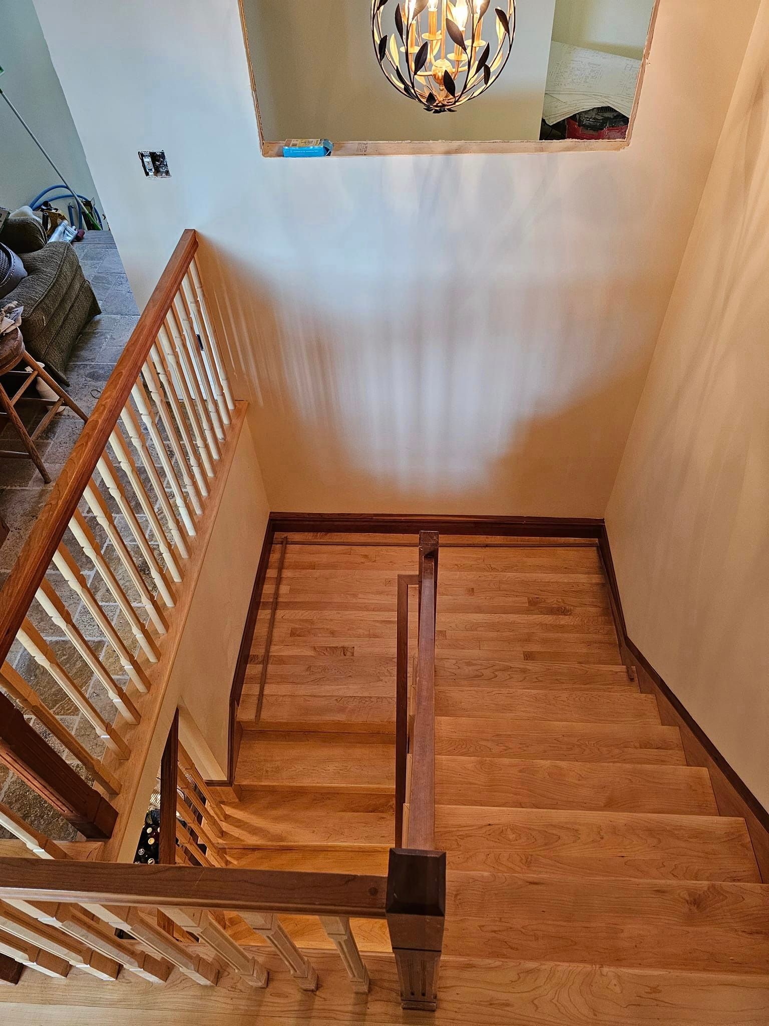 An aerial view of a wooden staircase in a house with a chandelier hanging from the ceiling.