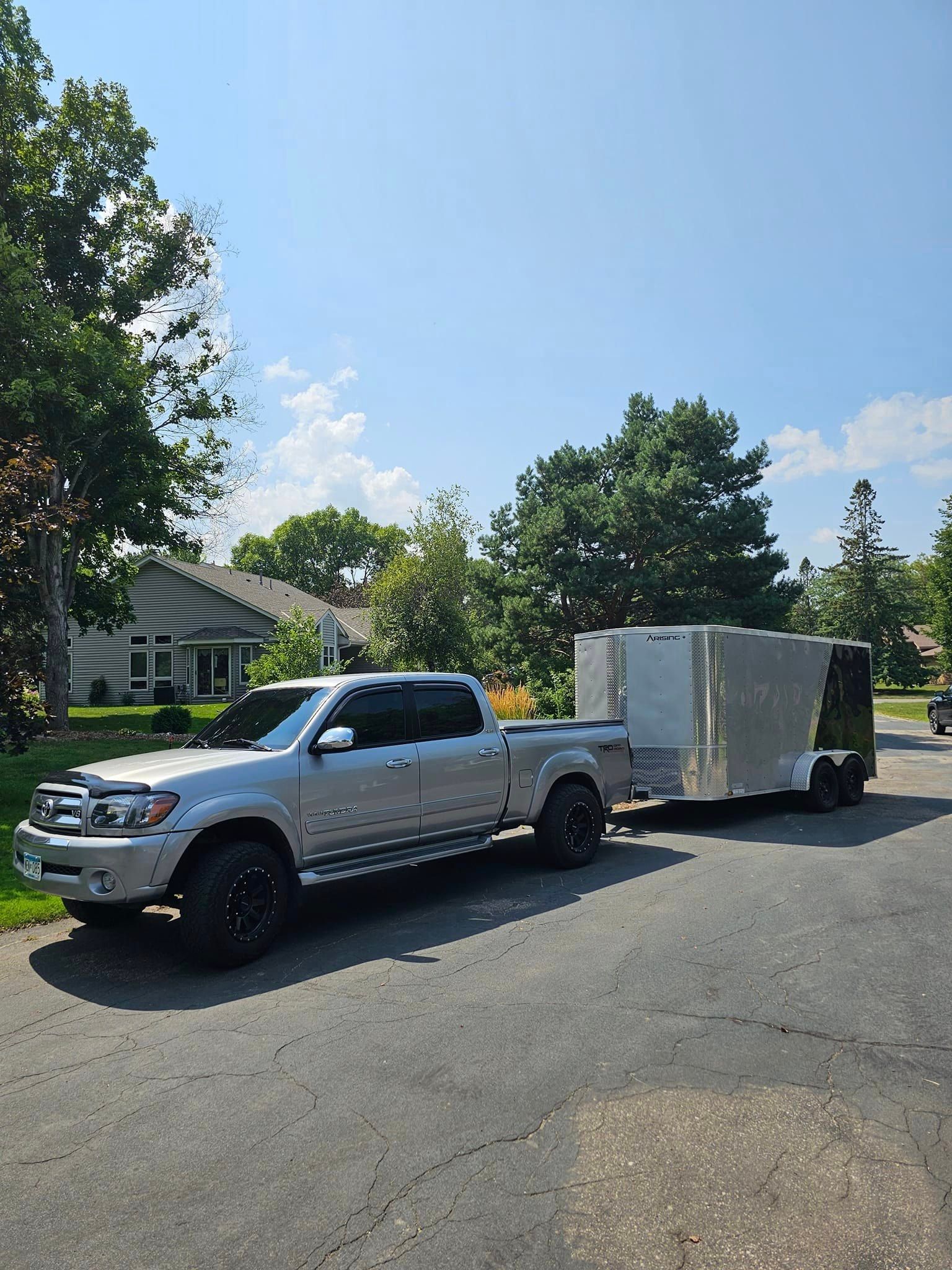 A silver truck with a trailer attached to it is parked on the side of the road.