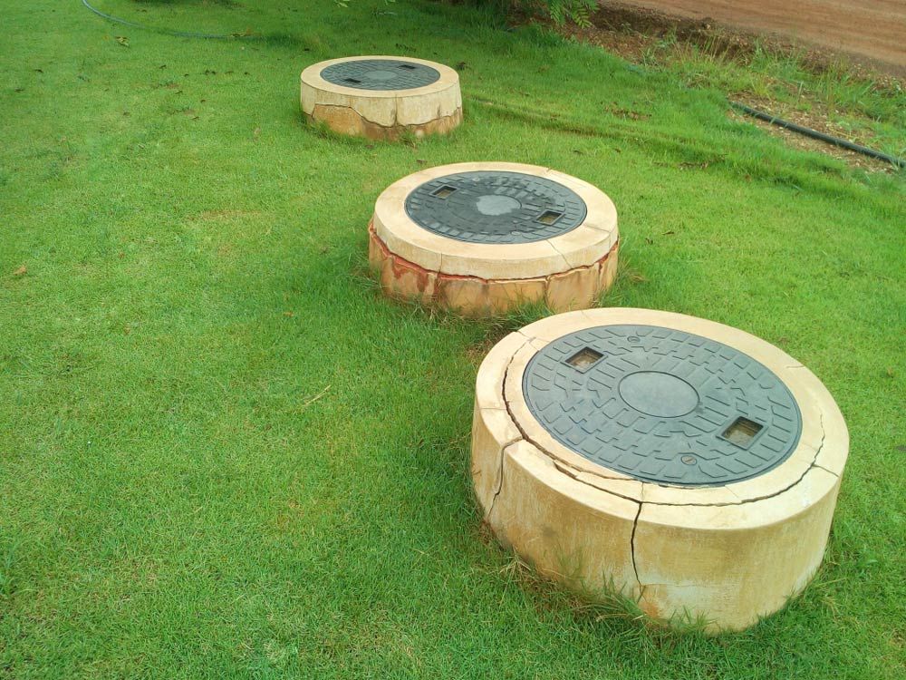 Three Manhole Covers Are Sitting on Top of a Lush Green Field — Cuttle Plumbing in Armidale, NSW