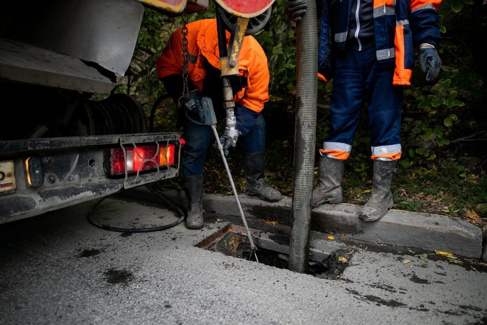 Two Men Are Working on a Manhole Cover With Drill Next to a Truck — Cuttle Plumbing in Armidale, NSW