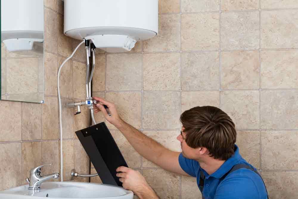 A Skilled Worker is Fixing a Water Heater in a Bathroom — Cuttle Plumbing in Armidale, NSW