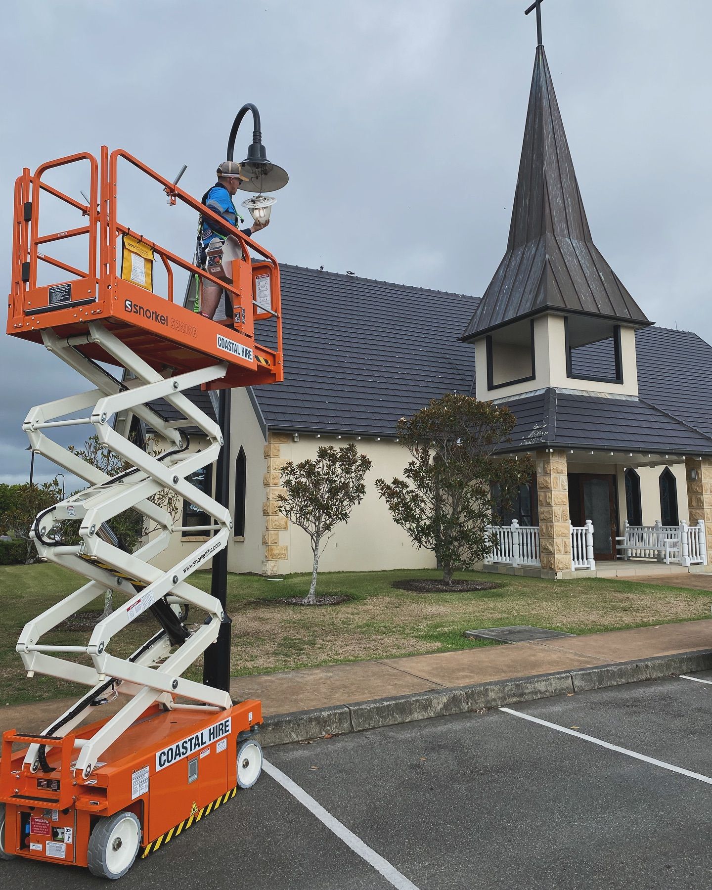 A Man is Standing on a Scissor Lift in Front of a Church — J T Walker Electrical In Gloucester, NSW