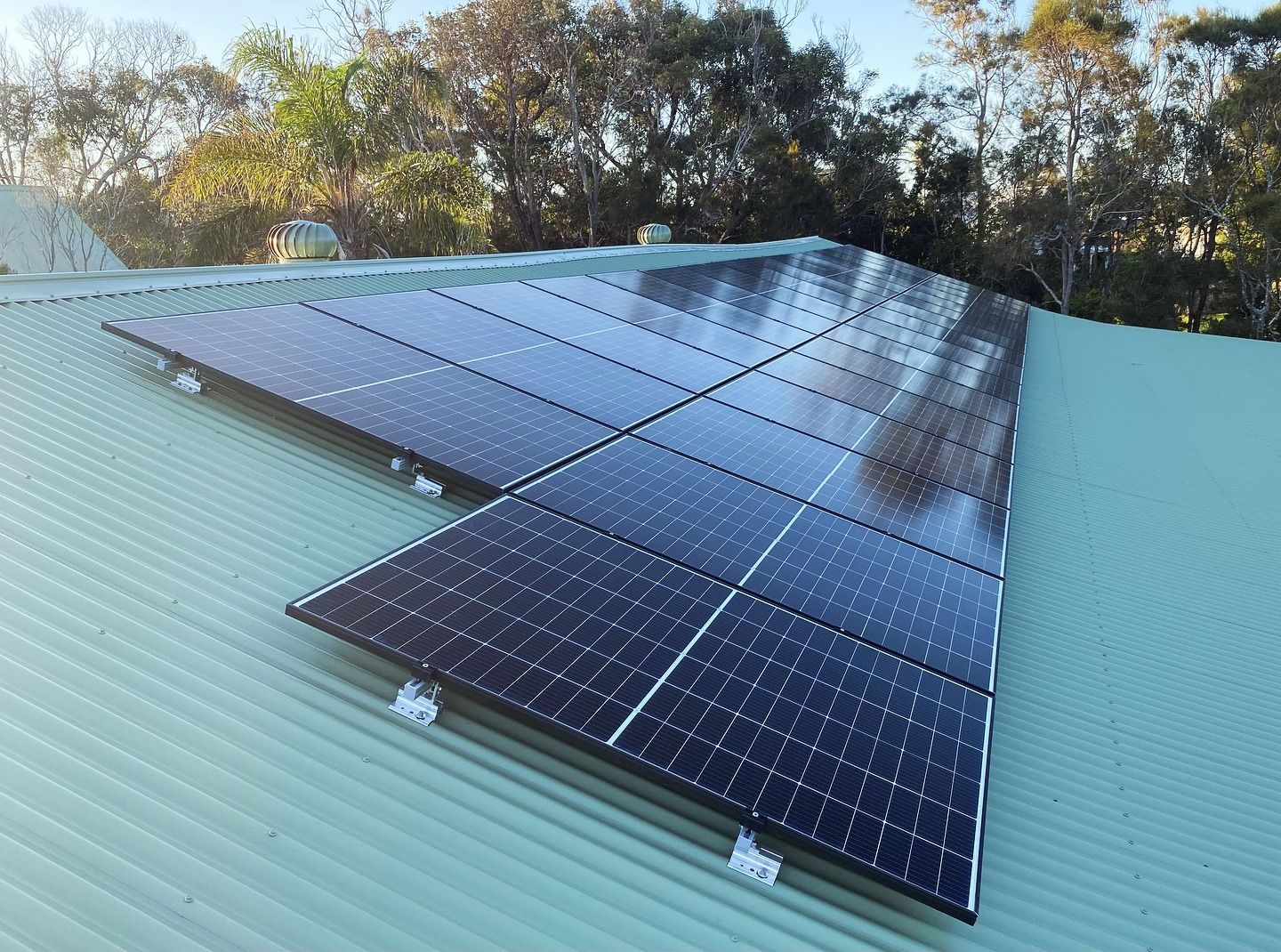 Solar panels installed on a green, corrugated metal roof, reflecting sunlight.