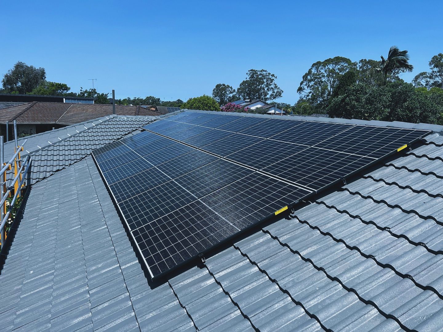 Solar panels installed on a gray tiled roof under a blue sky.
