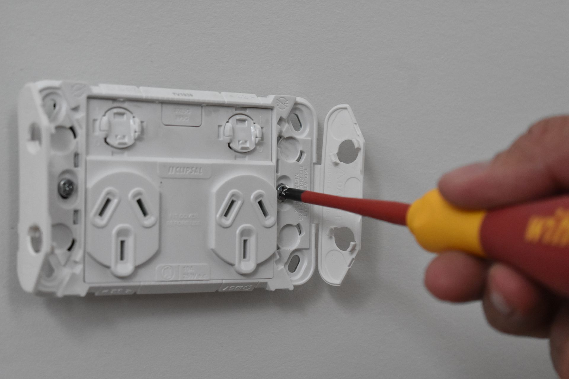 A person uses a screwdriver to secure a white electrical outlet to a wall.