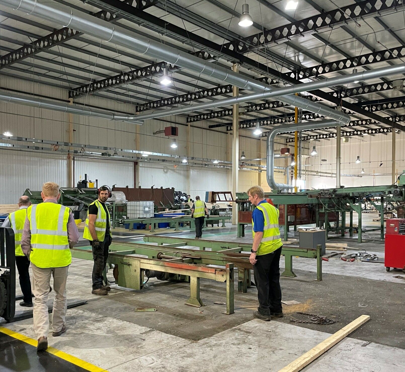 A group of men in safety vests are standing in a large factory.