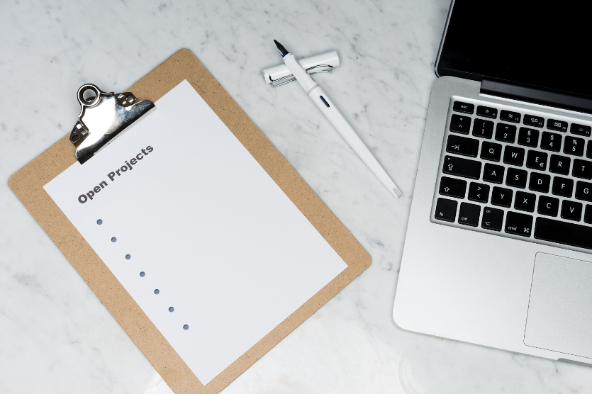 A clipboard with open projects written on it next to a laptop