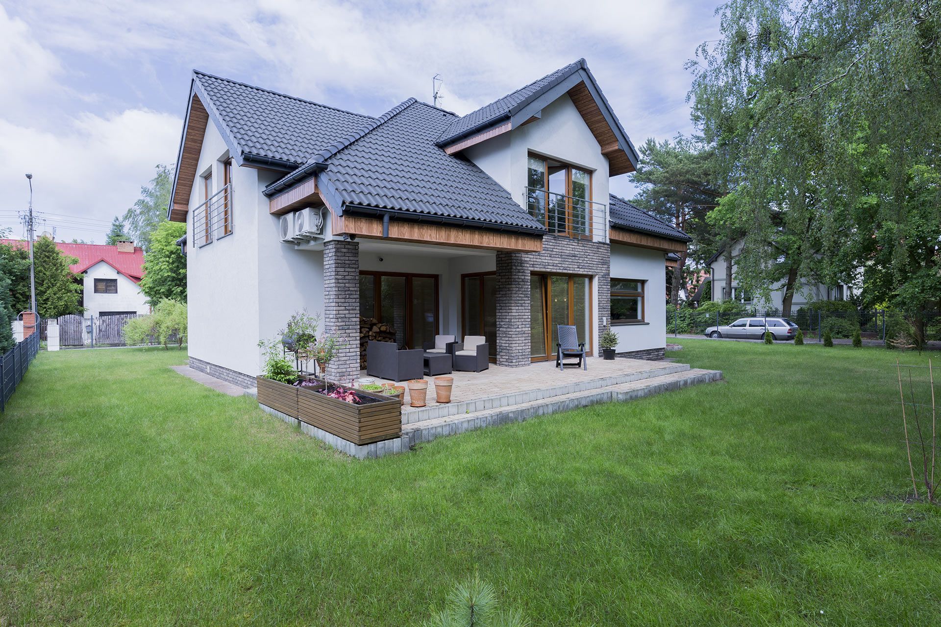 Two-story house with gray roof and light-colored siding. Lawn in front, small porch, trees.