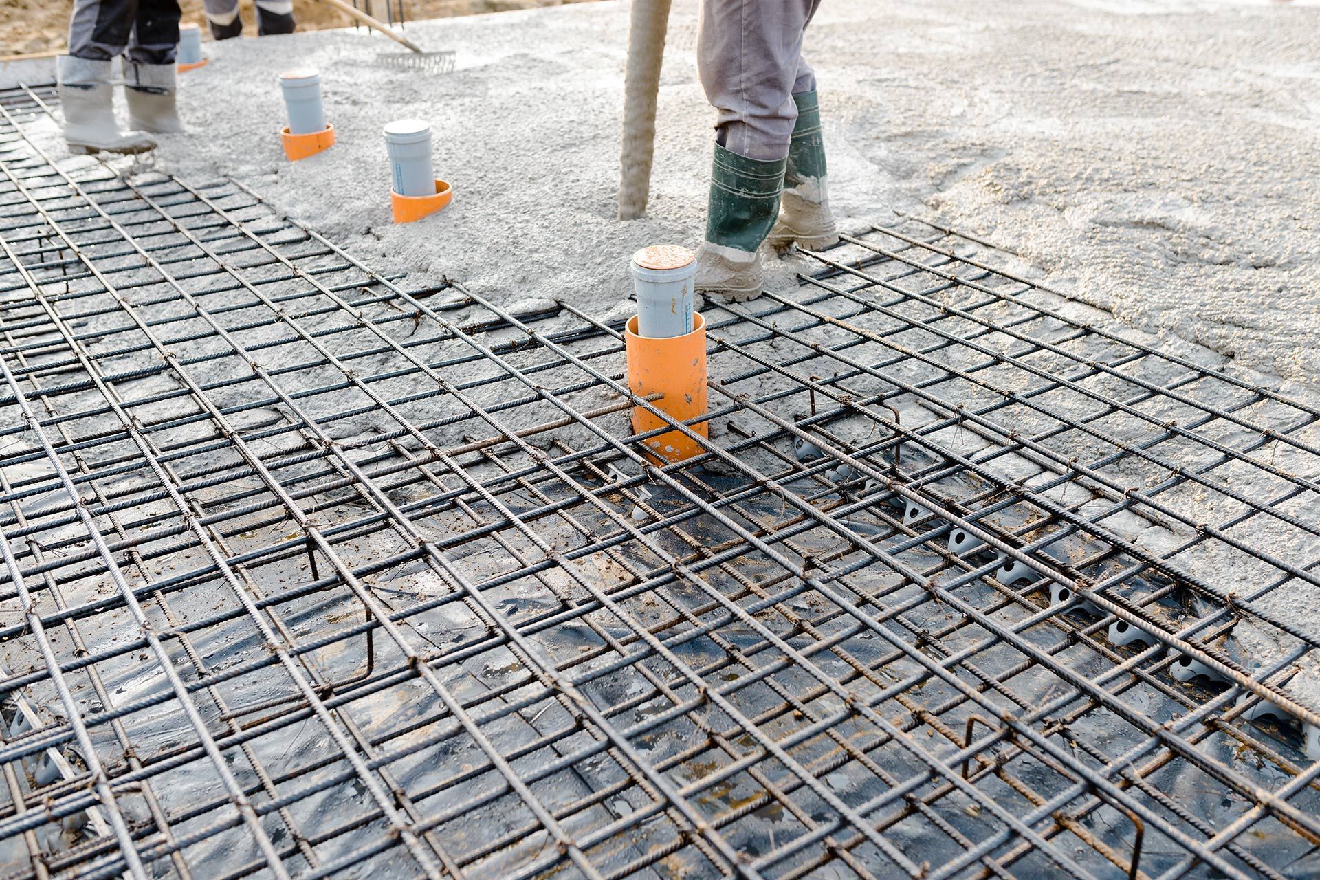 Construction site: concrete being poured over rebar grid, with workers in rubber boots.