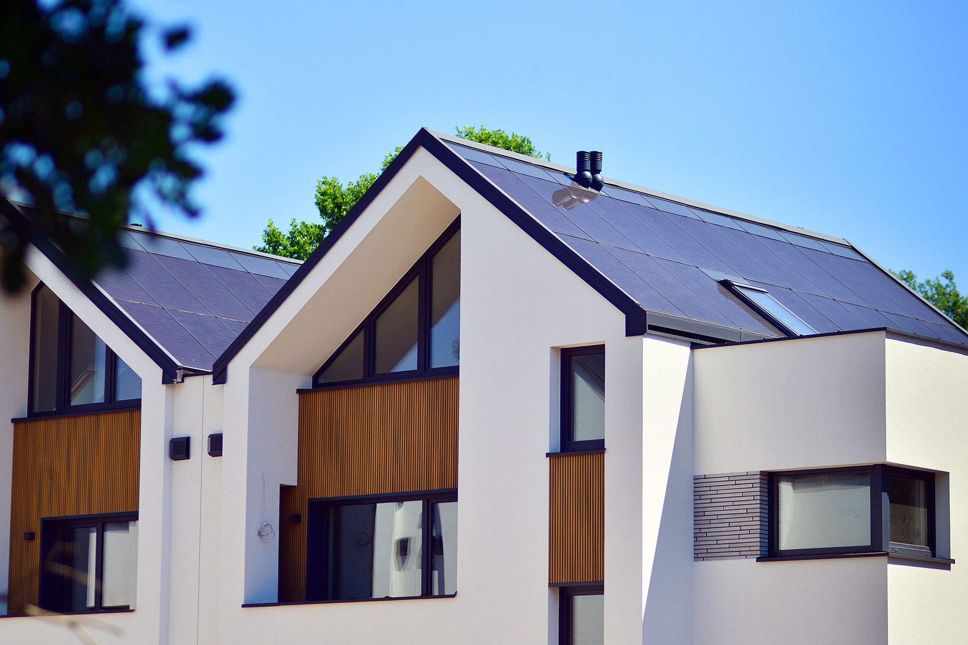 Modern white house with black roof and wooden accents against a blue sky.