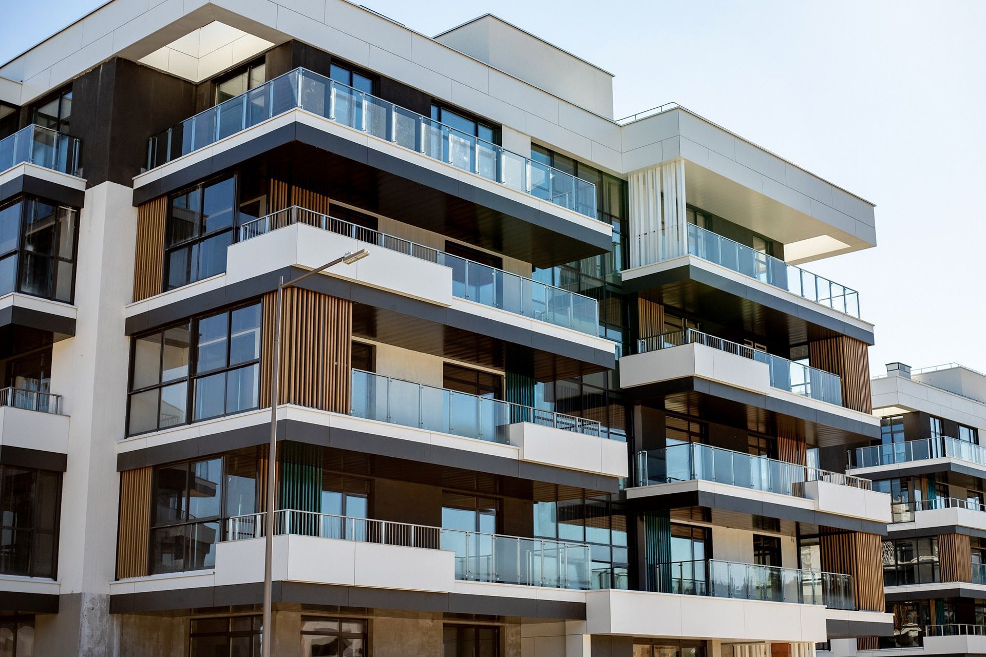 Modern apartment building with glass balconies and white and dark wood accents.