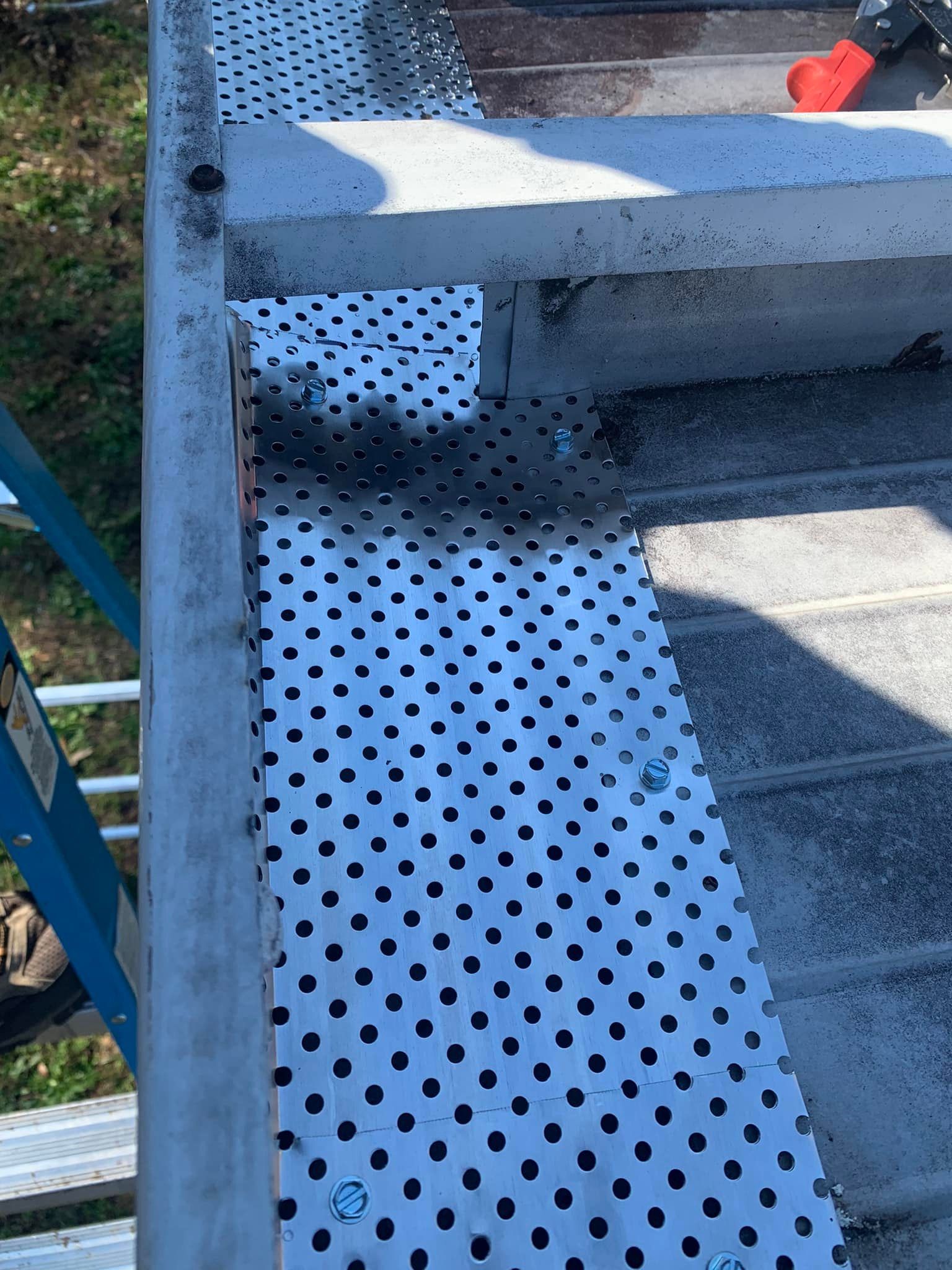 A person is working on a gutter with a ladder in the background
