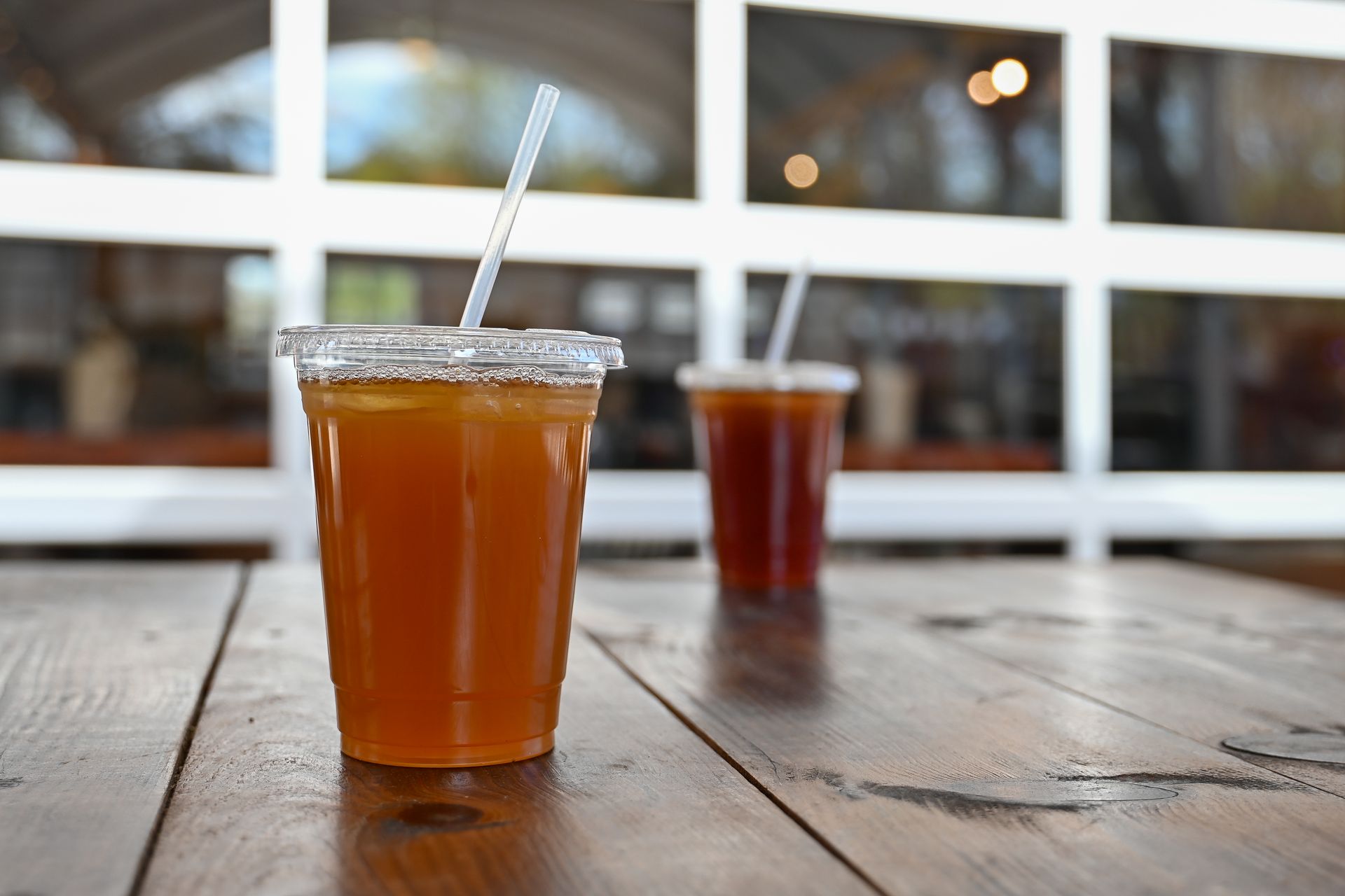 Two iced drinks in clear cups on a wooden table, in front of a window.