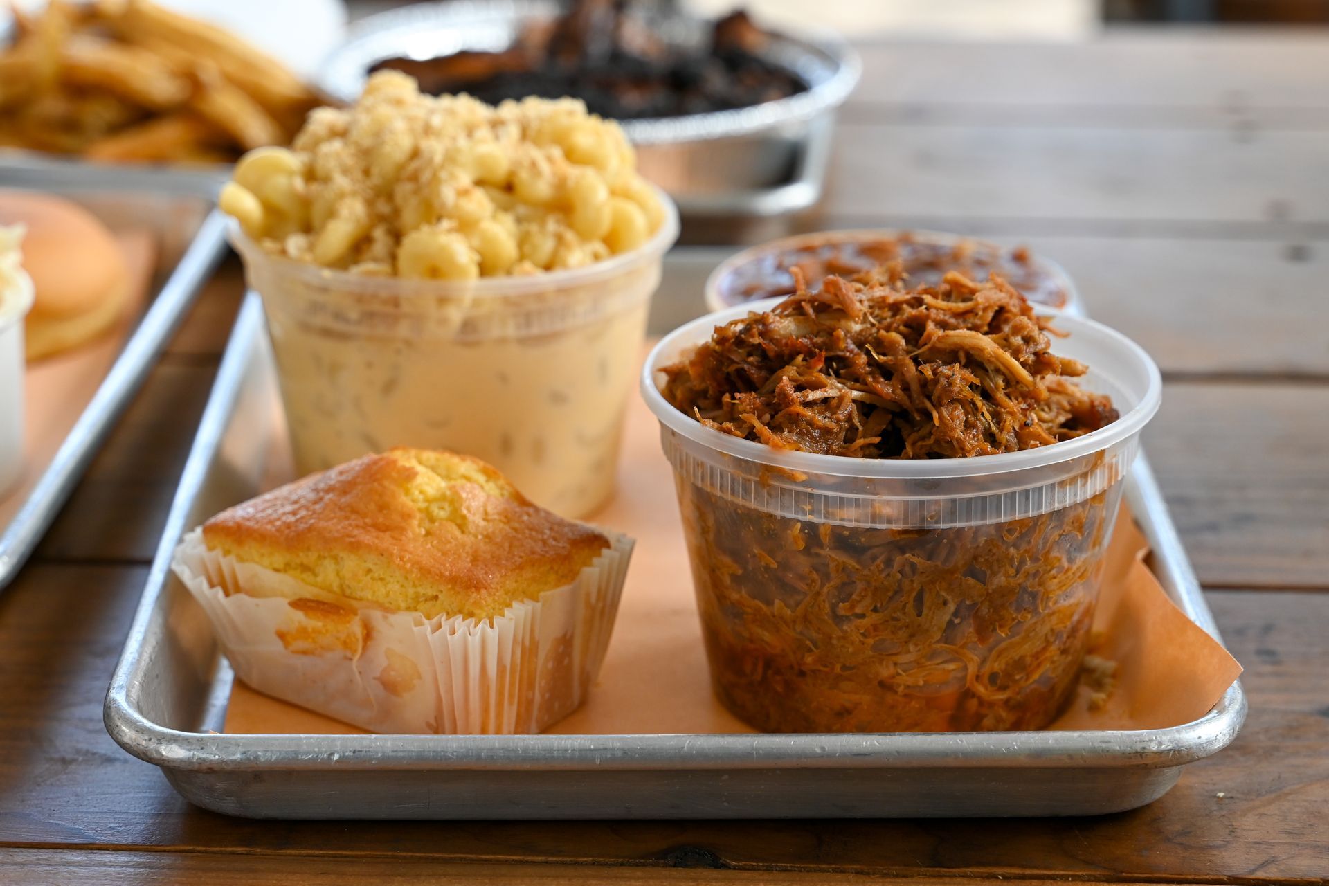 Tray of barbecue sides: mac and cheese, pulled pork, cornbread, and sides.
