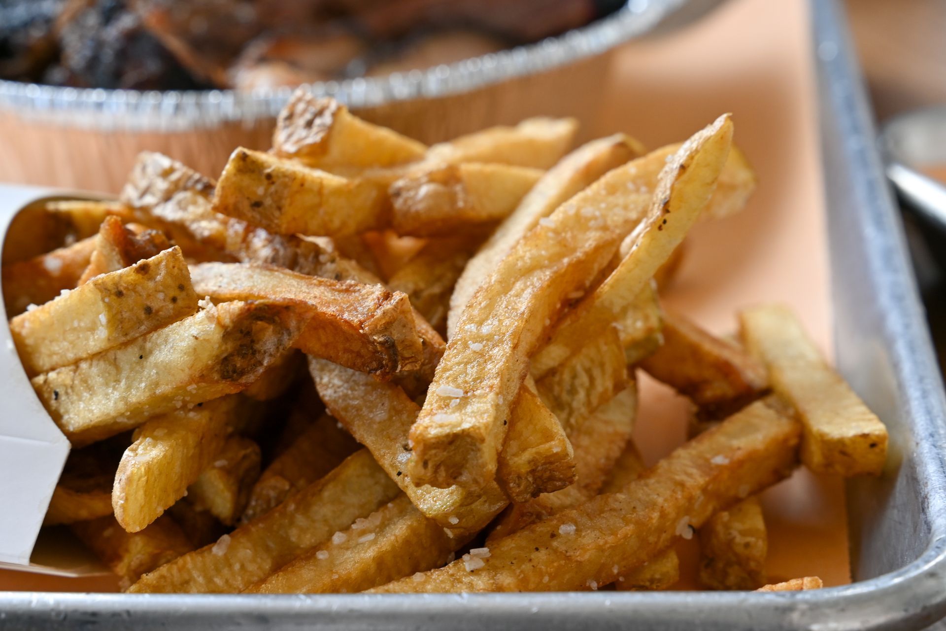 Pile of golden french fries on a metal tray, salt sprinkled.