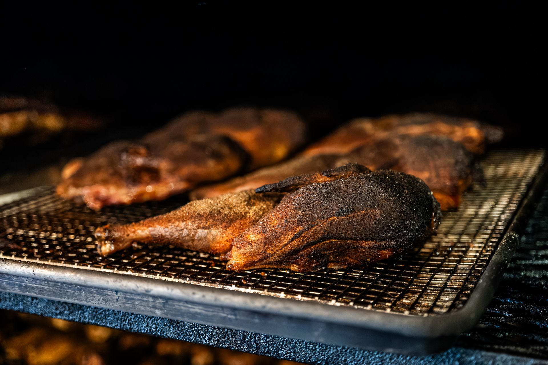 Smoked poultry on a wire rack inside a smoker. The skin is dark brown and crispy.