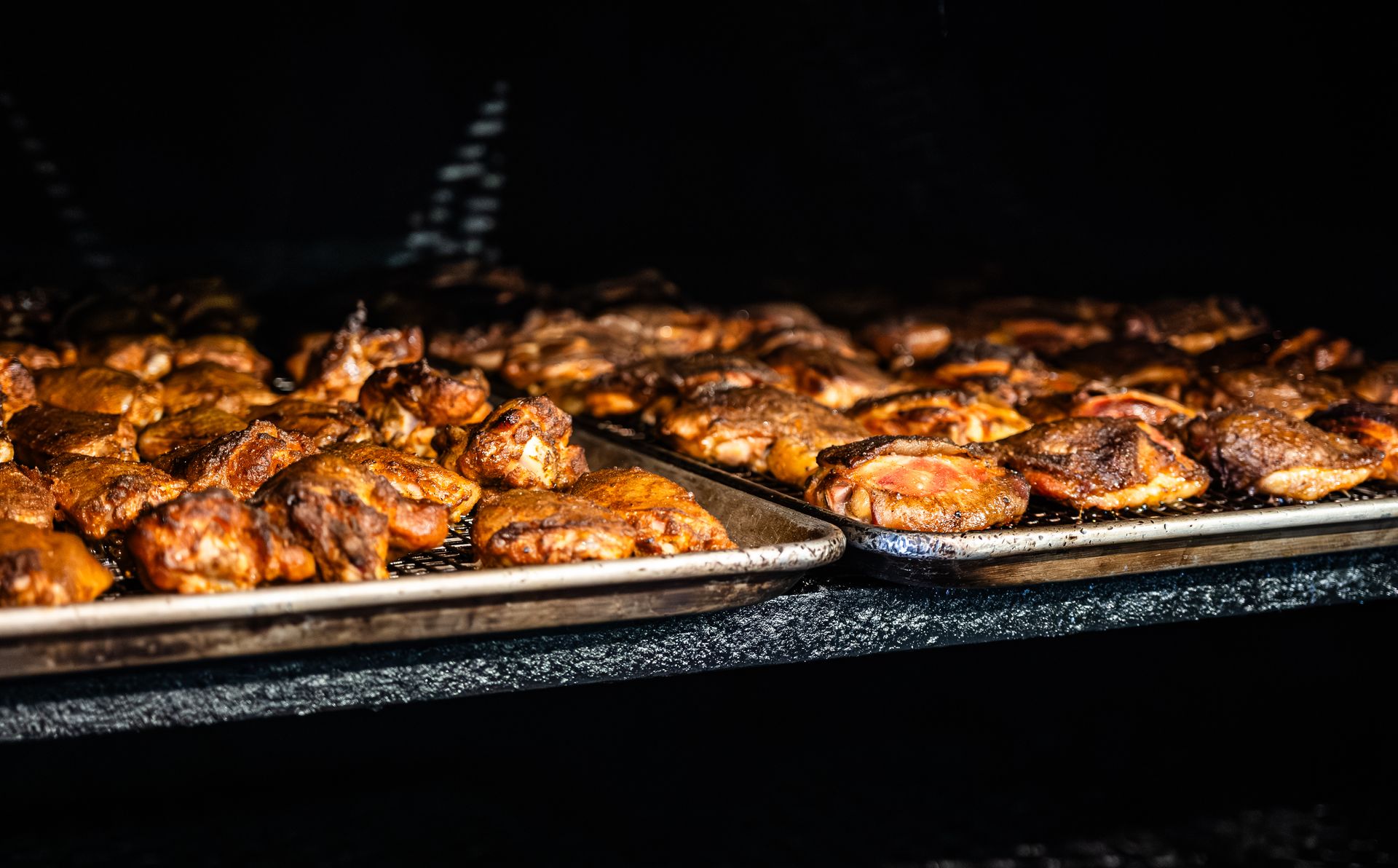 Chicken pieces on trays inside a smoker.