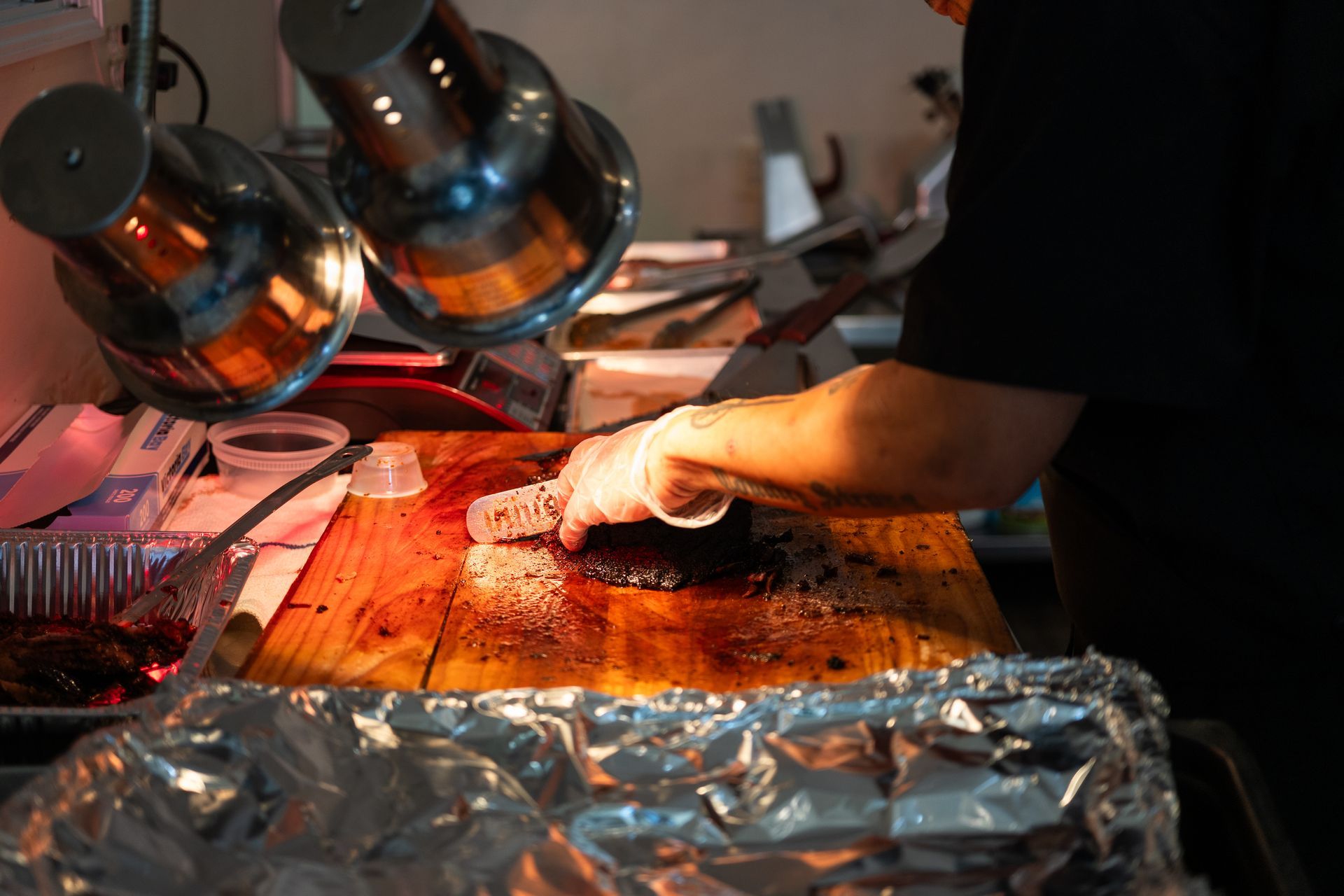 Person slicing meat on a wooden cutting board under warming lights