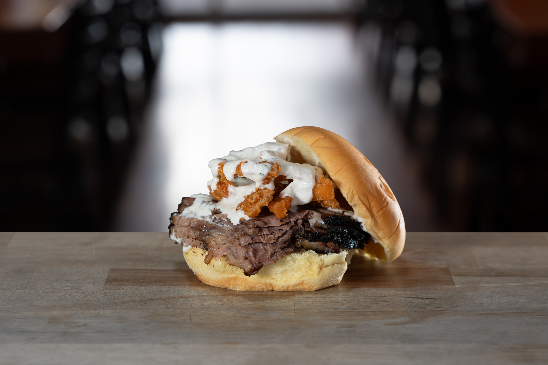 Sandwich with meat, sauce, and crispy topping on a wooden table.