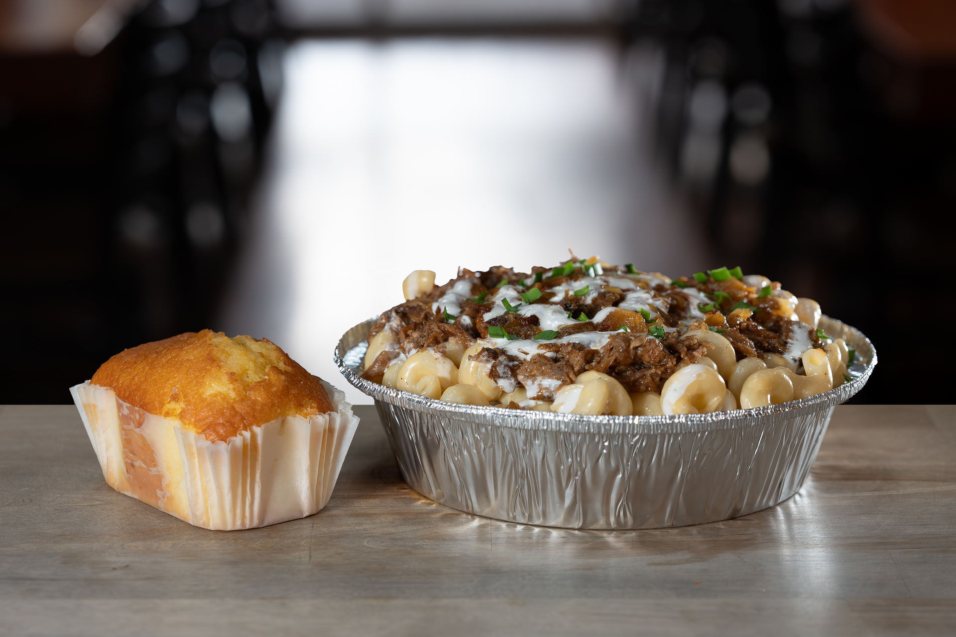 Mac and cheese bowl with toppings, next to a corn muffin. Set on a table.