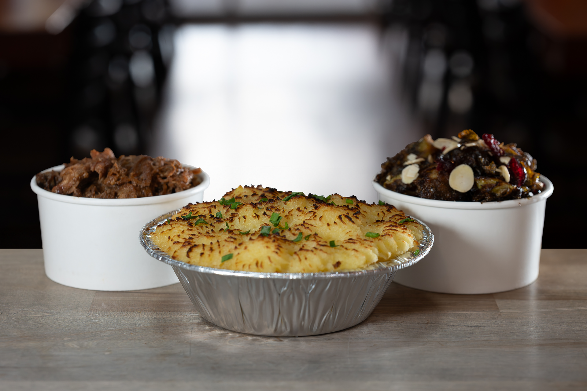 Three food dishes: a baked potato pie and two side dishes in white bowls.