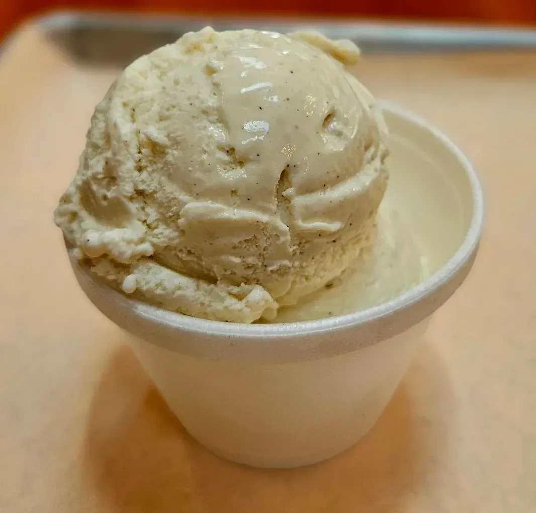 Vanilla ice cream in a white paper cup, on a light-colored surface.