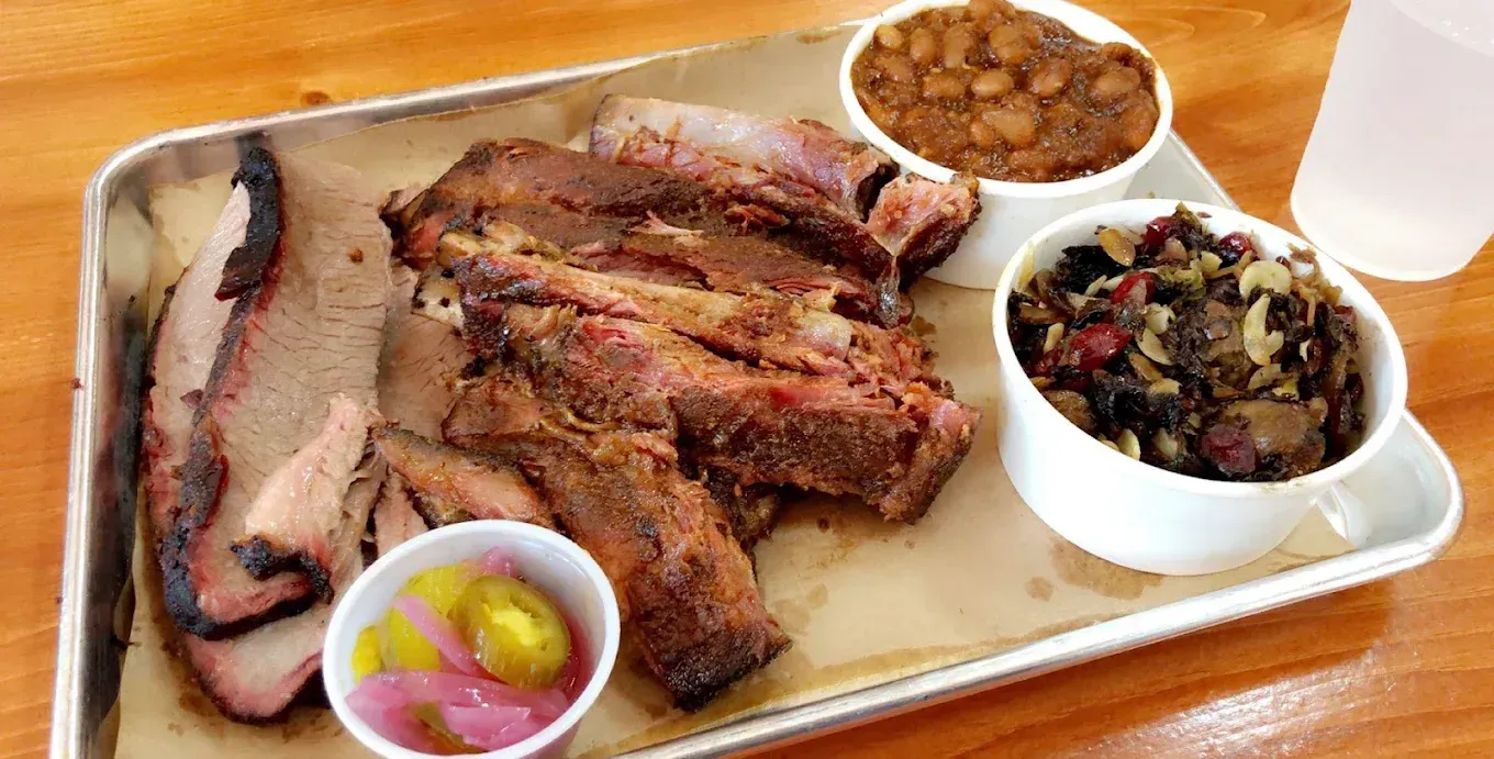Barbecue platter with brisket, ribs, beans, coleslaw, and pickles.