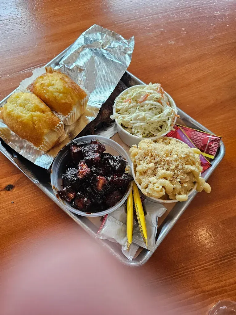 BBQ tray with cornbread, coleslaw, mac and cheese, and meat on a wooden table.