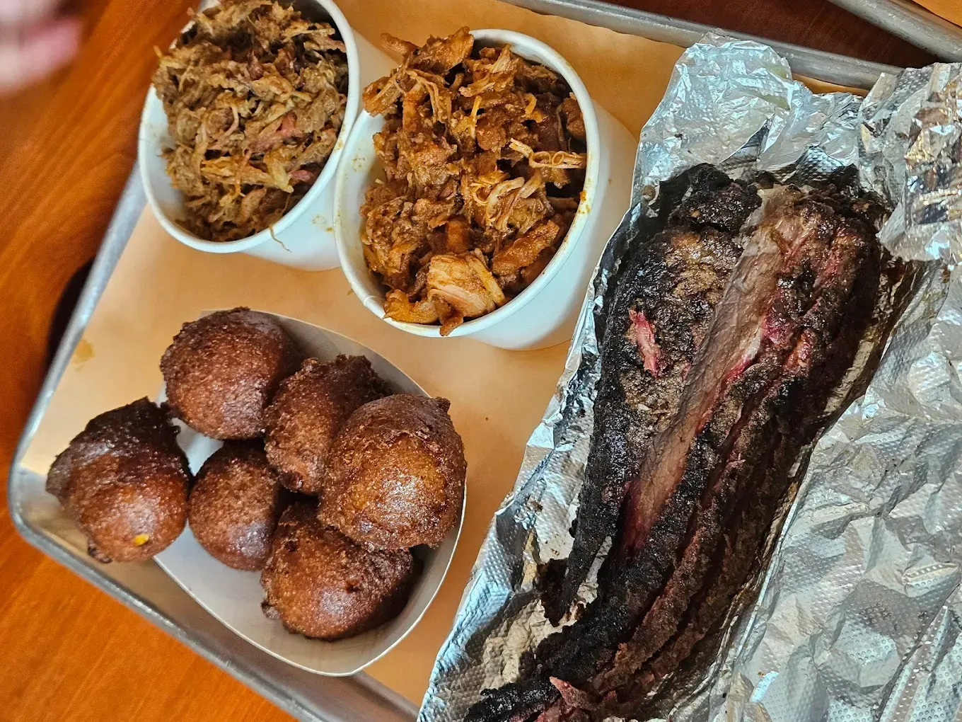Barbecue platter: pulled pork, brisket, and hushpuppies on a metal tray.