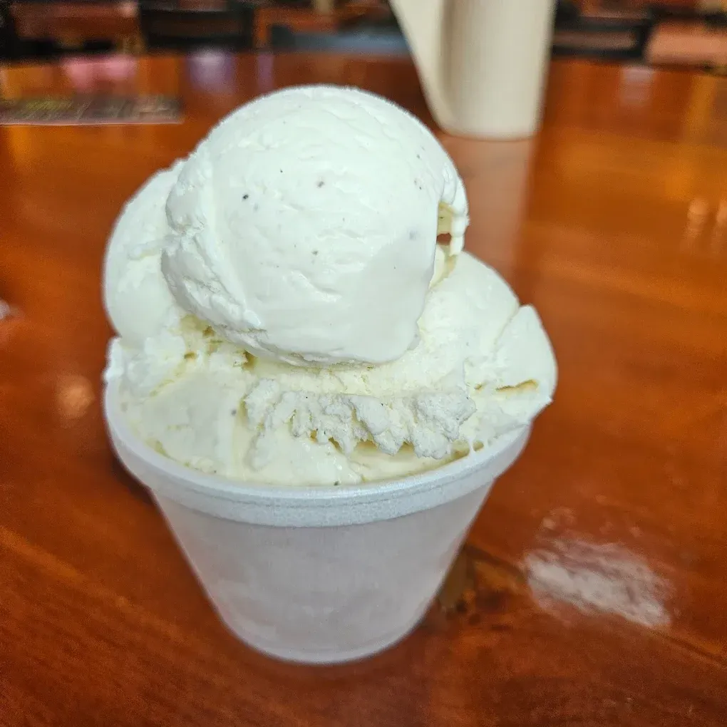 Three scoops of white ice cream in a white cup on a wooden table.